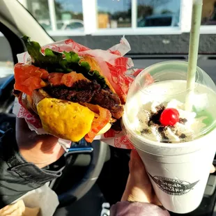  a hand holding a sandwich and a drink