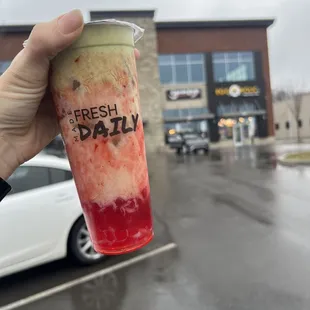 a hand holding a drink in a parking lot