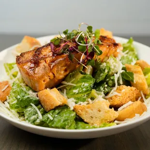 a plate of salad with salmon and croutons