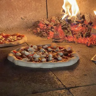two pizzas being cooked in a brick oven
