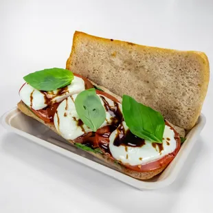 Baked Caprese Sandwich Layered with Fresh Basil Leaves, Tomatoes, Fresh Mozzarella and Balsamic Glaze on Toasted Noble Ciabatta Bread.