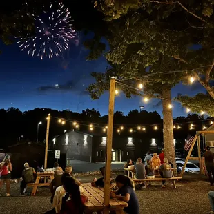 people sitting at picnic tables and fireworks in the sky