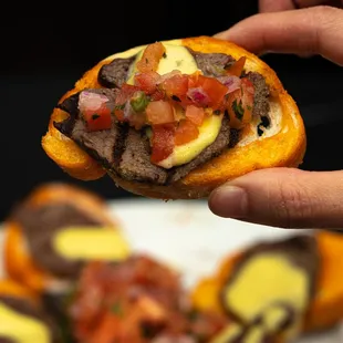a hand holding a hamburger with cheese and tomato