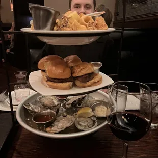  a man sitting at a table with three plates of food and a glass of wine