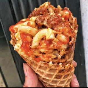 a hand holding a waffle cone filled with macaroni and cheese