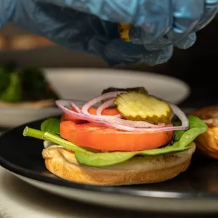 a person putting a pickle on a sandwich