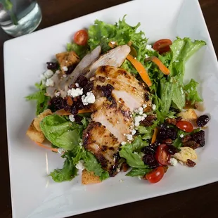 a salad with chicken, lettuce, tomatoes, cranberries, and feta cheese