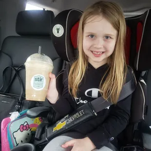 a girl in a car seat holding a drink