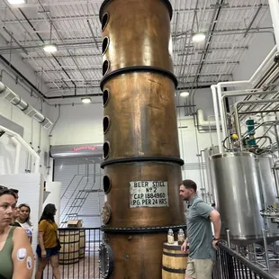  a man and a woman standing in front of a large copper vessel