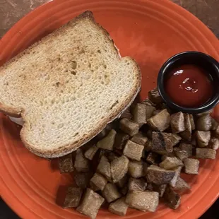 a plate with a sandwich, potatoes and ketchup