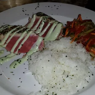 Sesame crusted seared Ahi Tuna with wasabi aoli drizzle, jasmine rice, and Asian slaw.