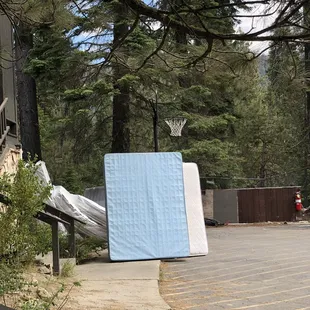 Mattresses piled up in the parking lot in the dirt. Some of them look new wrapped in plastic???