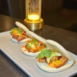 PORK BELLY BAO Sweet glazed crispy pork belly, spicy gochujang aioli, cucumber, and shaved carrots and scallions in a fluffy steamed bao bun