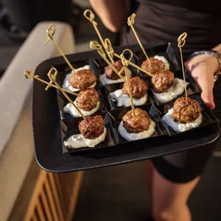 a woman holding a tray of meatballs