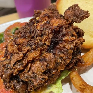a fried chicken sandwich with lettuce, tomato, and onion rings