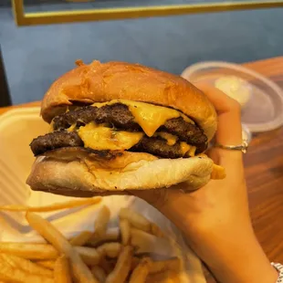 a hand holding a cheeseburger and fries