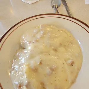 Biscuit and gravy. Sausage and scrambled eggs in background.