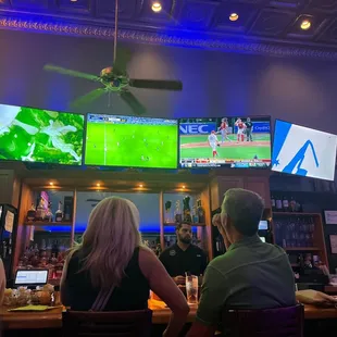 people sitting at a bar watching televisions