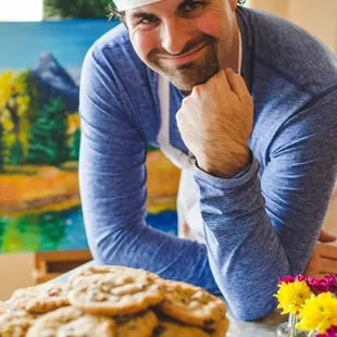 a man in a chef&apos;s hat leaning over a table with a cookie