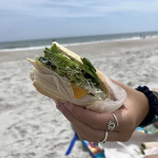 a person holding a sandwich on the beach