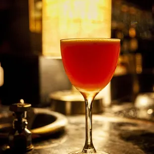 a red drink in a wine glass on a bar