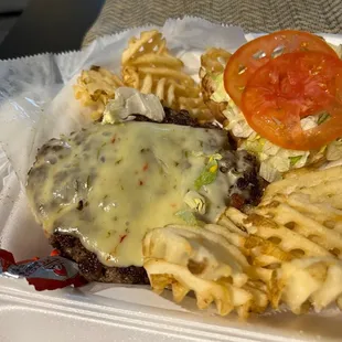 a hamburger, fries, and tomato on a styrofoam container