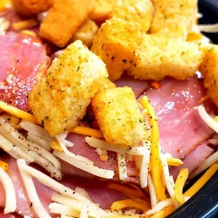a plate of spaghetti, ham, cheese, and croutons