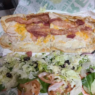 a sub sandwich and salad on a wrapper