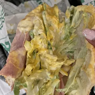 a hand holding a sandwich with lettuce and ham