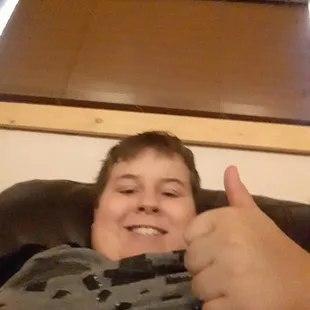 a boy laying in a chair with his thumb up