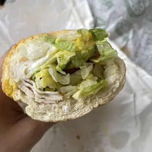 a hand holding a sandwich with lettuce and cheese