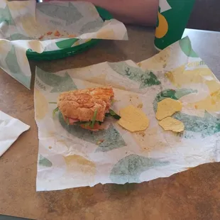 a person sitting at a table with a sandwich and chips