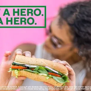 a woman holding a sandwich in front of a pink background