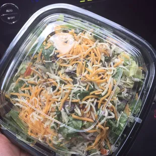 a hand holding a salad in a plastic container