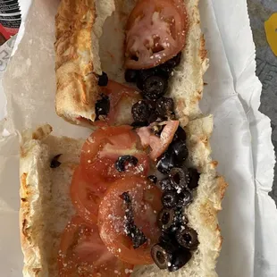 a half eaten sandwich with tomatoes and olives