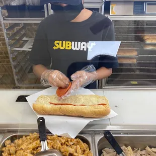a person in a mask putting a hot dog on a bun