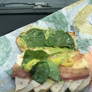 a sandwich with bacon, avocado, and spinach