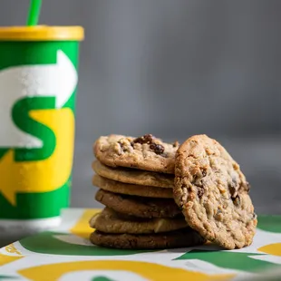 a stack of chocolate chip cookies next to a cup of soda