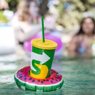 a cup of watermelon drink on a floatie in a pool