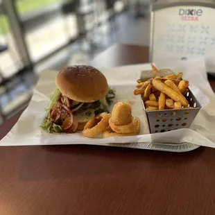 burger with fried egg on top with tomato lettuce onions seasoned French fries and onion rings and with a fountain drink