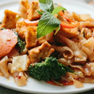 Tofu Drunken Noodles: Flat rice noodles stir-fried with chicken and vegetables in a basil sauce. Gluten Free and Vegan Available