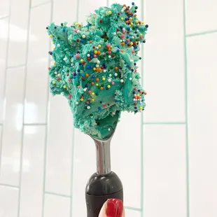 a hand holding a candy scooper with sprinkles on it