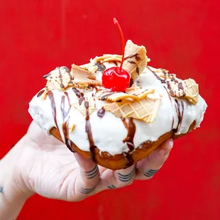 a hand holding a donut with a cherry on top