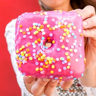 a woman holding a pink donut with sprinkles