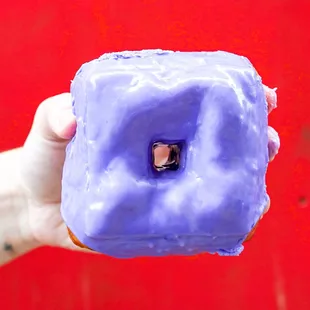 a hand holding a purple frosted donut