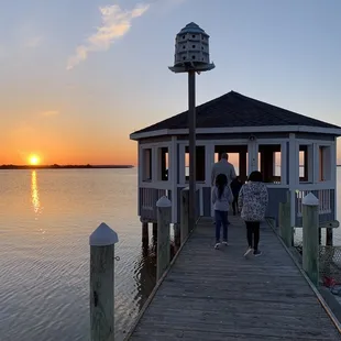 two people walking on a dock at sunset