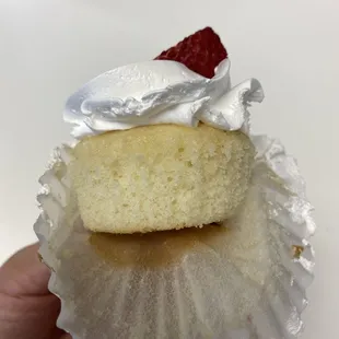 a hand holding a cupcake with whipped cream and a strawberry on top