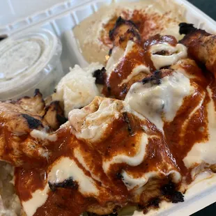 Chicken Kabob with sauce a little hot sauce, side of taziki and hummus. Under here are garlic potatoes and rice. A full plate!