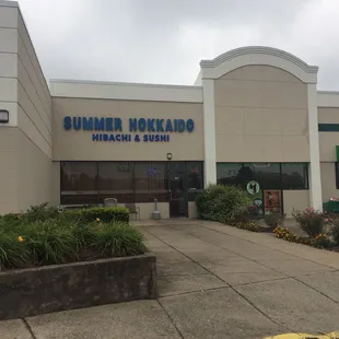 Restaurant front in a strip mall nestled between a Dollar Tree and a gym.