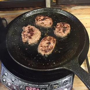 four burgers cooking in a grill pan